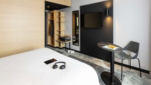 Een moderne hotelkamer met een bed, een bureau met stoel, een televisie en een kledingkast.