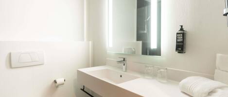 A modern bathroom with a white sink, a mirror, a towel, and a bottle of shampoo.