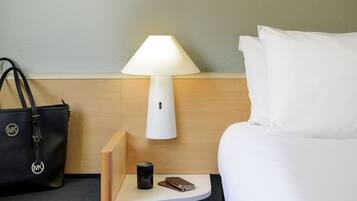 Une chambre d’hôtel avec un lit, une table de chevet avec une lampe, une machine à café, un téléphone intelligent et un sac à main noir.
