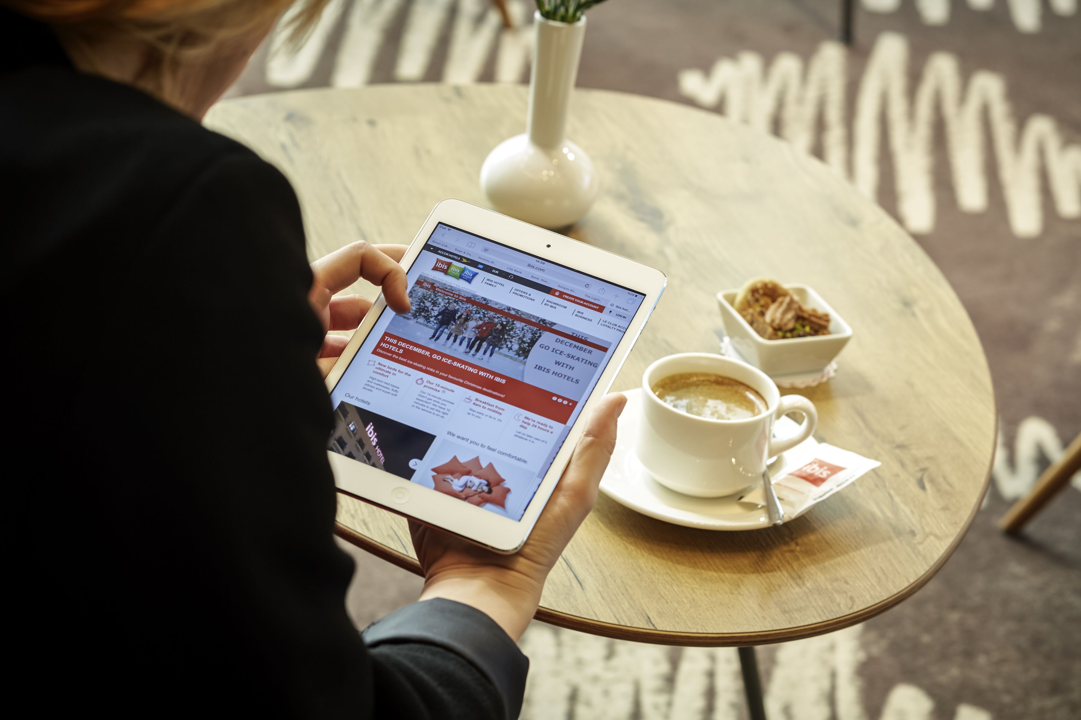 A person using a tablet at a round table with a cup of coffee and a small bowl of sugar.