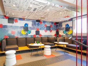 A modern lounge area with a mural, seating, and a staircase. - ibis Mulhouse Ile Napoléon (Sausheim)