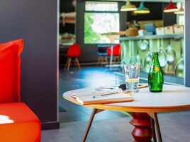 Una mesa con un cuaderno, un vaso y una botella verde en un interior moderno con sillas rojas y una zona de bar.