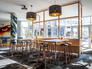 A modern cafe interior with wooden tables and chairs, large windows, and hanging pendant lights. - ibis Styles Paris Bercy (Paris)