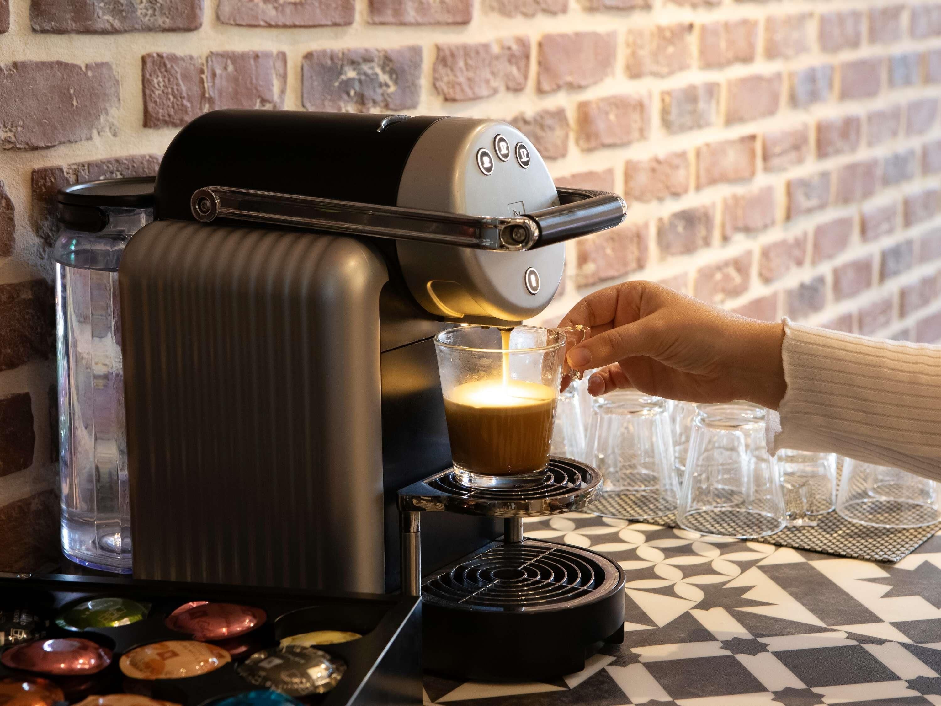 A coffee machine dispensing coffee into a cup, with a brick wall in the background.