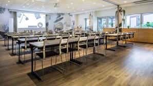 A conference room with multiple tables and chairs, a projector screen, and a large window with a view of the outside. - ibis Styles Paris Bercy (Paris)