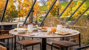 An outdoor dining area with tables and chairs, a view of trees and a building structure in the background. - ibis Styles Paris Bercy (Paris)
