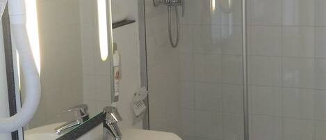 Un baño moderno con un lavamanos blanco, un espejo, ducha con cerramiento de vidrio y una toalla colgada en la pared.