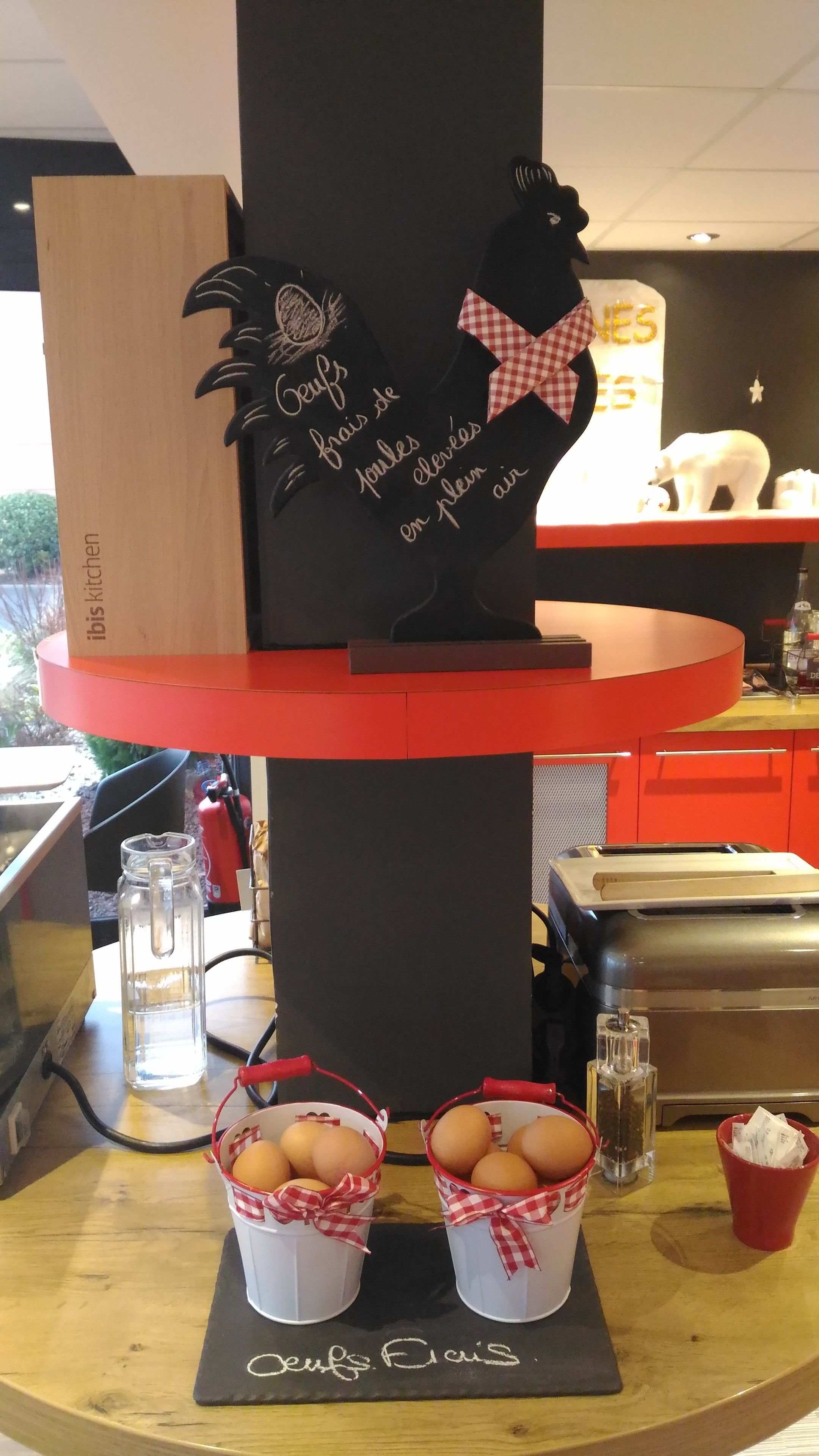 A kitchen counter with a black and red appliance, two baskets of eggs, and a decorative sign with a rooster and text.