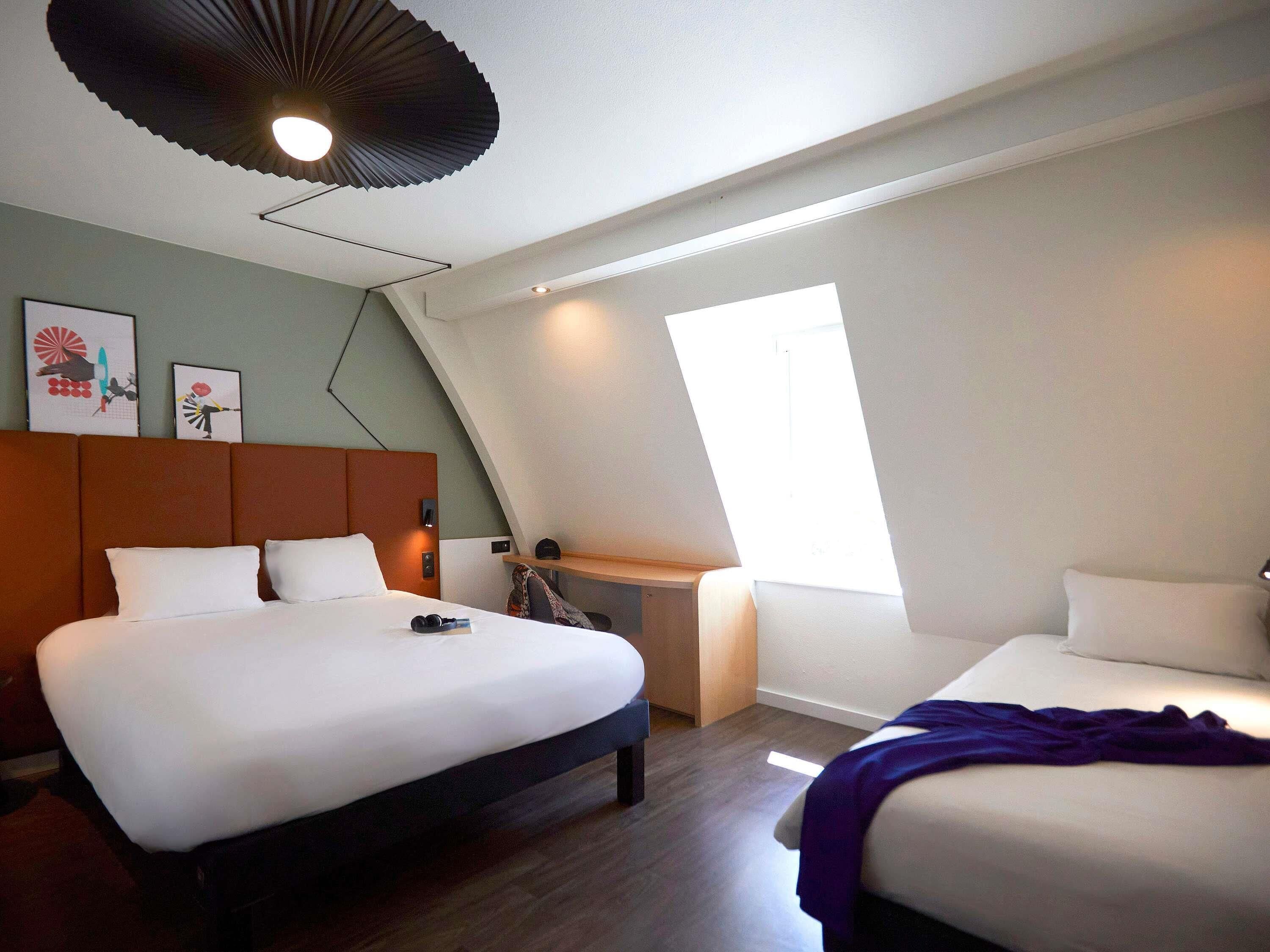 A modern hotel room with a large bed, a smaller bed, a desk, and a ceiling fan.