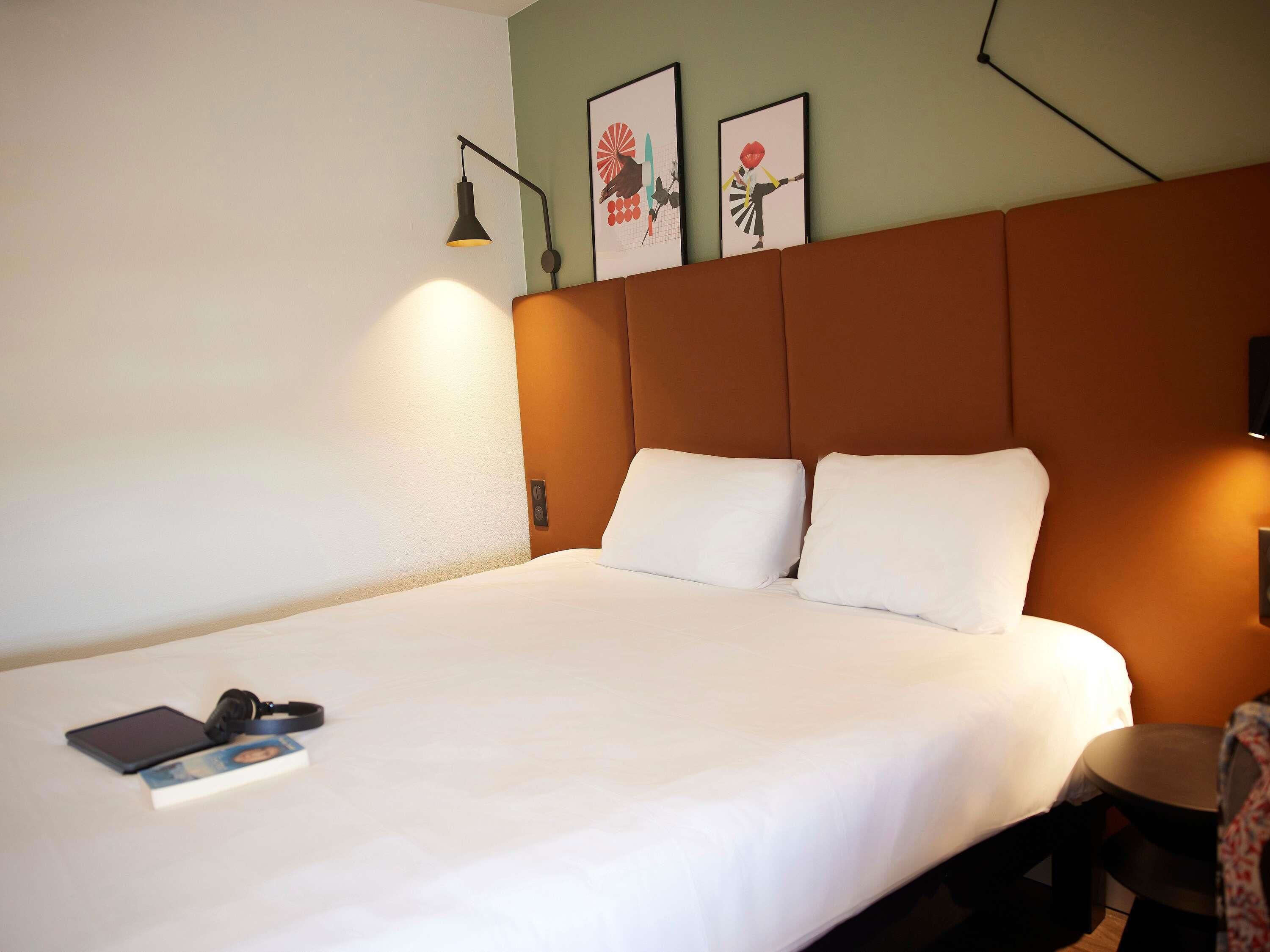 A hotel room with a large bed, a bedside table with a lamp, and two framed pictures on the wall.