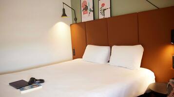 A hotel room with a large bed, a bedside table with a lamp, and two framed pictures on the wall.