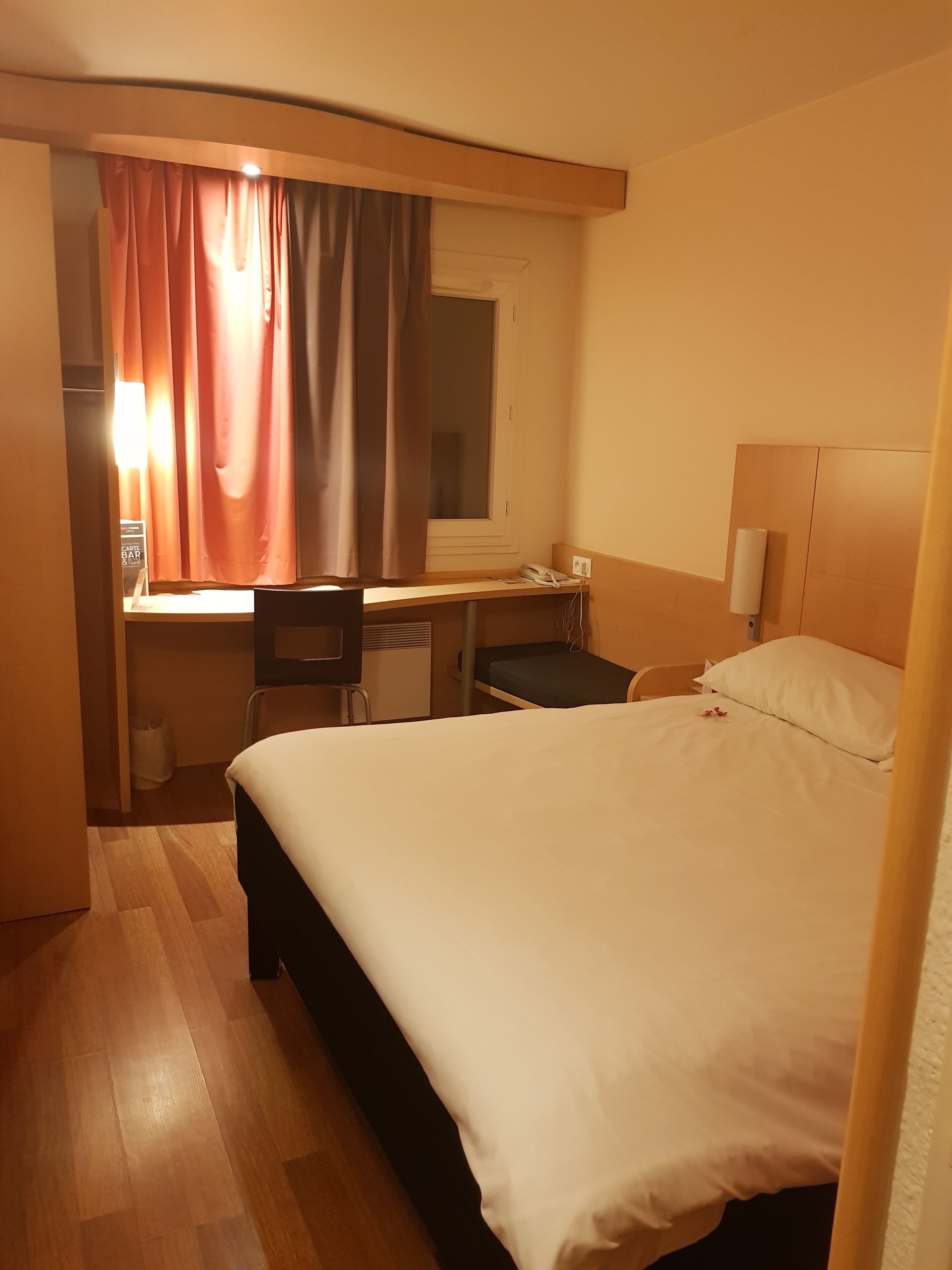 A hotel room with a bed, desk, chair, and a window with curtains.