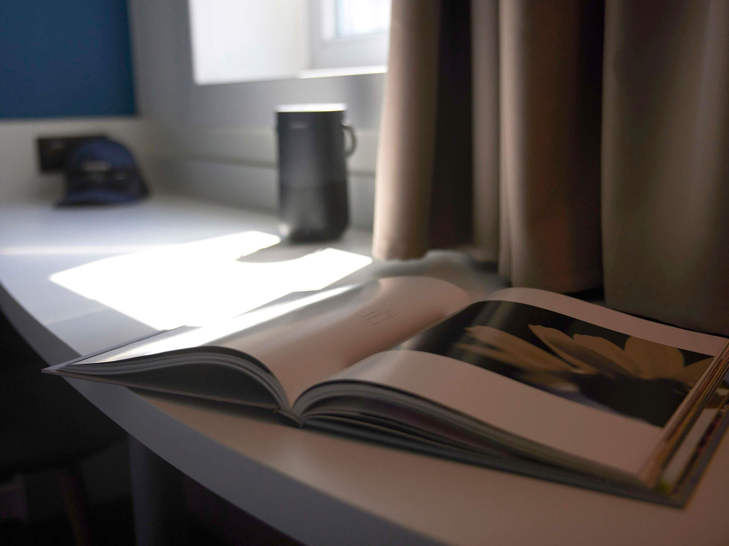An open book on a table with a window and curtains in the background.