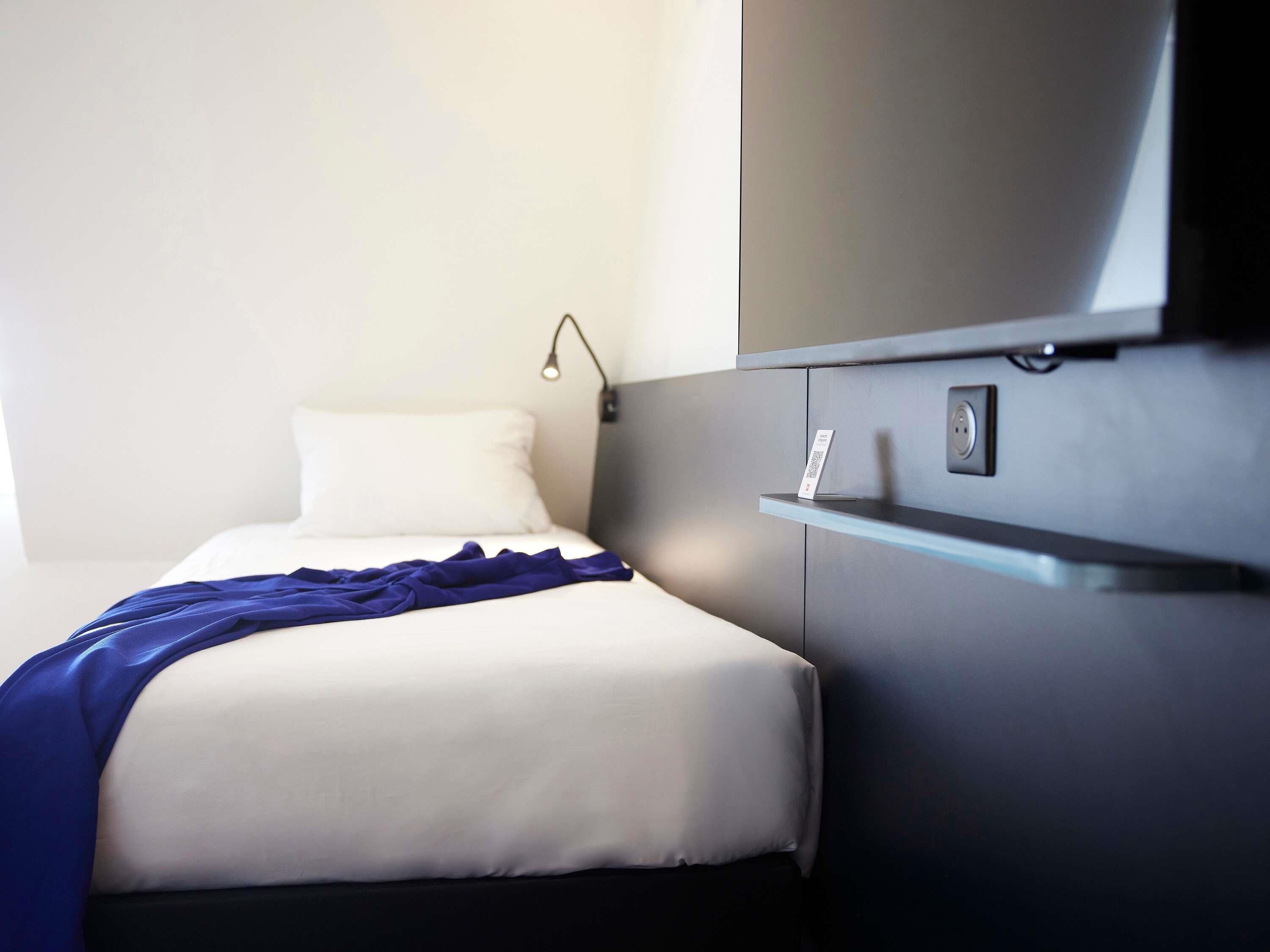 Habitación de hotel con cama, mesita de noche, televisor montado en la pared y toma de corriente.