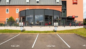 A modern hotel with a prominent 'ibis HOTEL' sign, a curved glass facade, and a parking lot with marked spaces. - ibis Chalon-sur-Saone North (Chalon-sur-Saone)