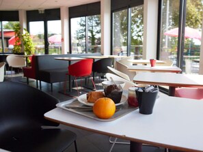An outdoor café with tables and chairs, a tray with food and a drink, and a view of the outside. - ibis Chalon-sur-Saone North (Chalon-sur-Saone)