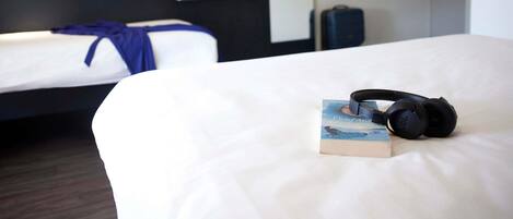 Una habitación de hotel con una cama, un libro, audífonos, una maleta y un televisor.
