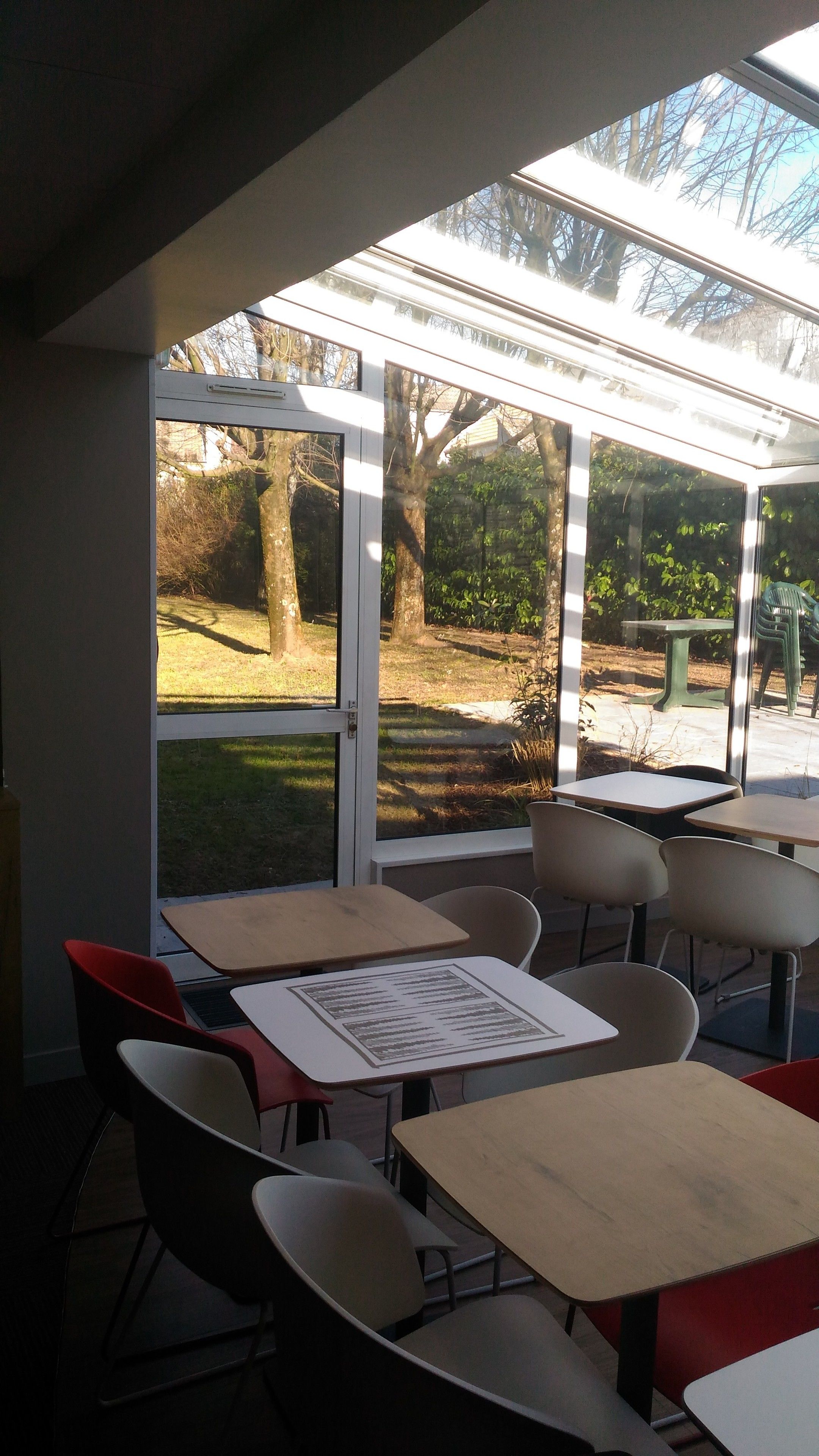 A room with tables and chairs, large windows with a view of trees and grass outside.