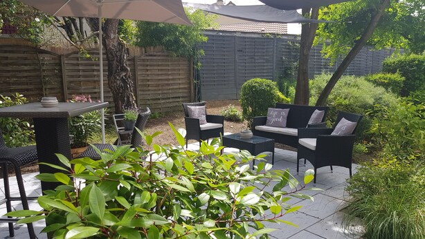 An outdoor patio with a table and chairs, surrounded by greenery and a wooden fence. - ibis Chalon-sur-Saone North (Chalon-sur-Saone)