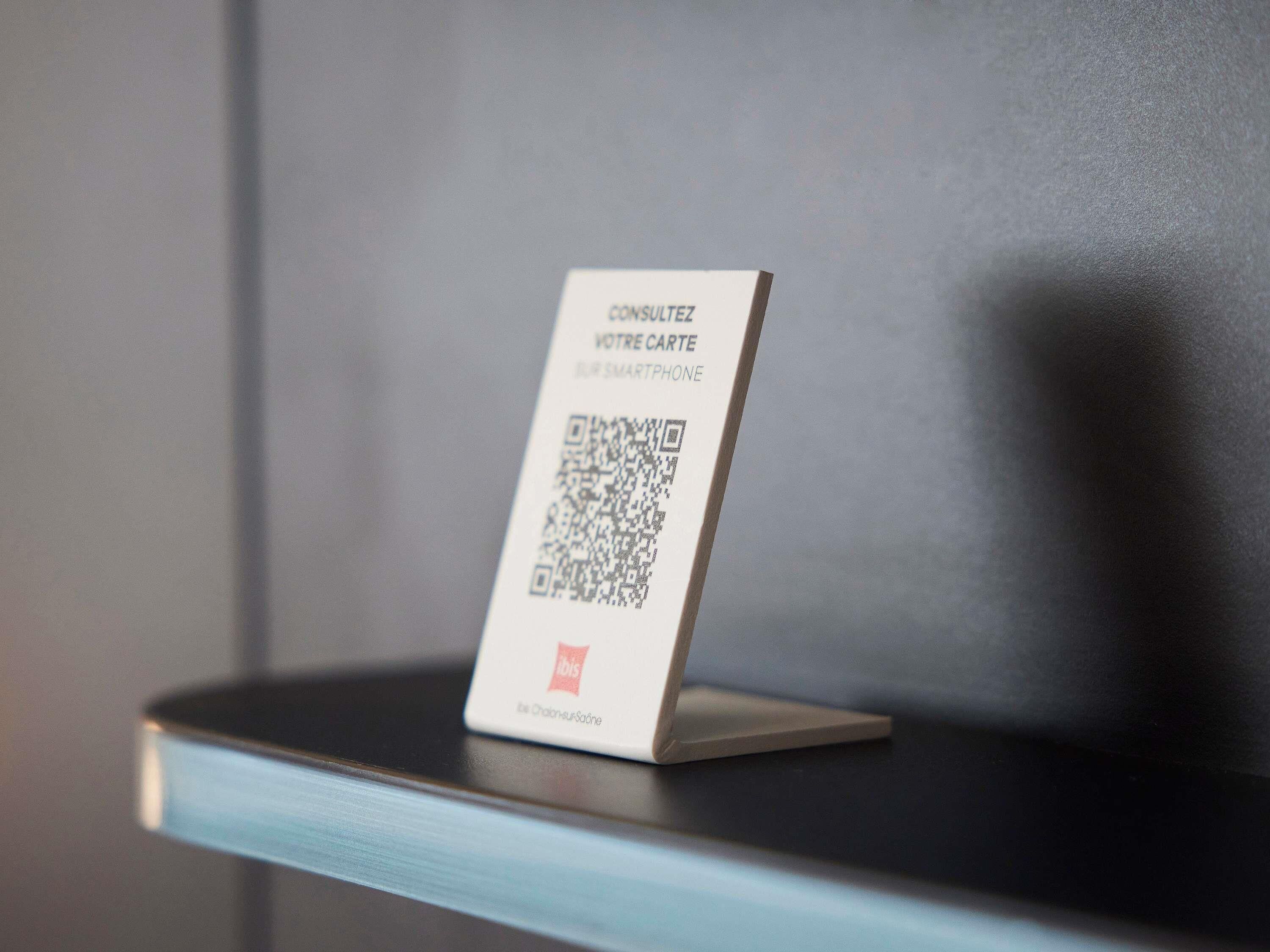 Ein QR-Code auf einem weißen Schild mit französischem Text, platziert auf einer dunklen Oberfläche.