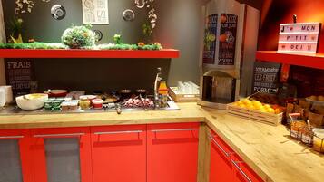 Una barra de desayuno con una máquina de café, una exhibición de frutas y diversos alimentos.