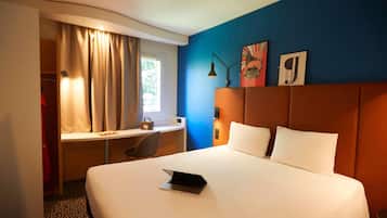 A hotel room with a bed, a desk, a chair, a laptop, and a window with curtains.