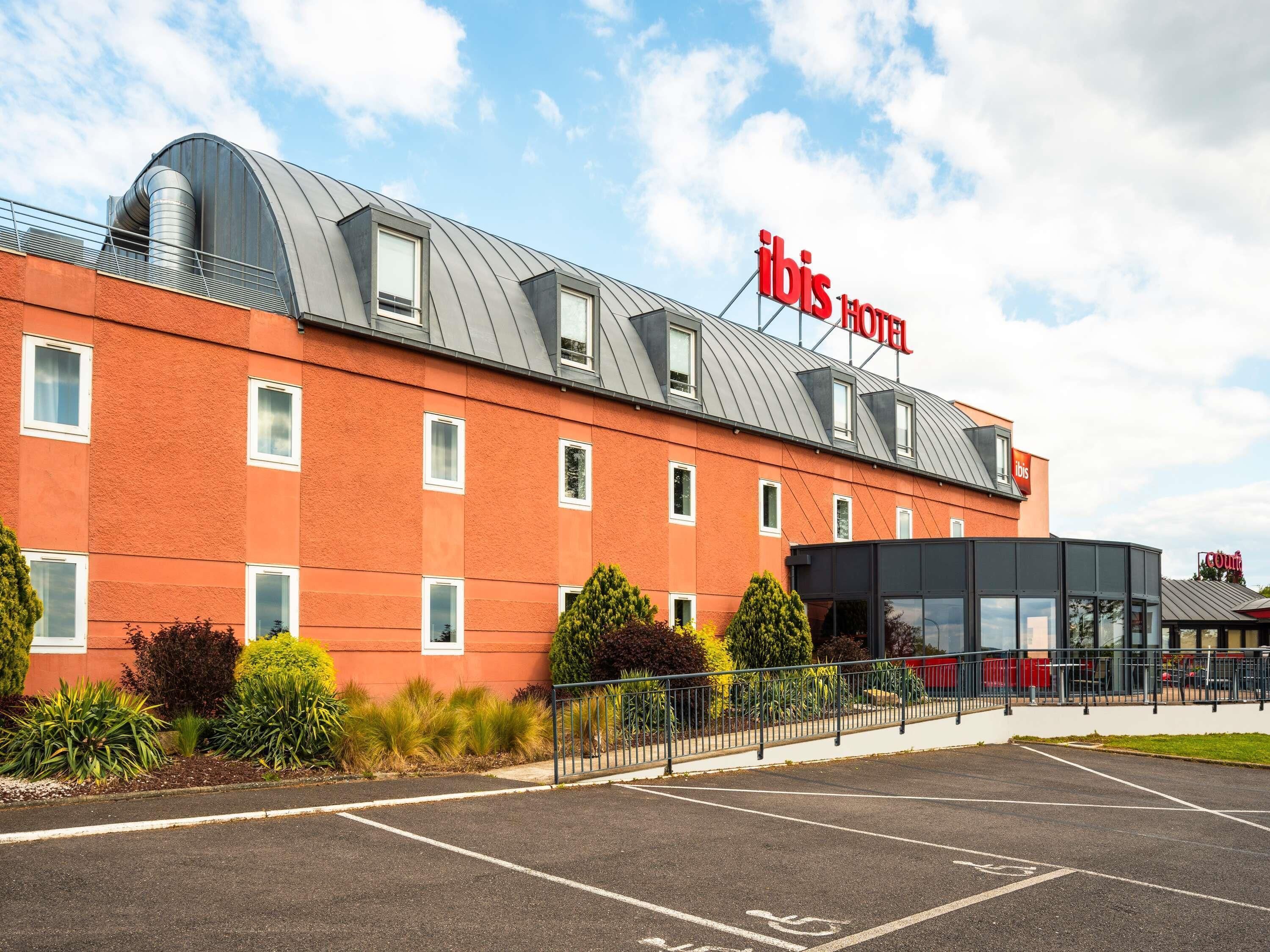 A hotel with a red facade, a prominent 'ibis Hotel' sign, and a parking lot.