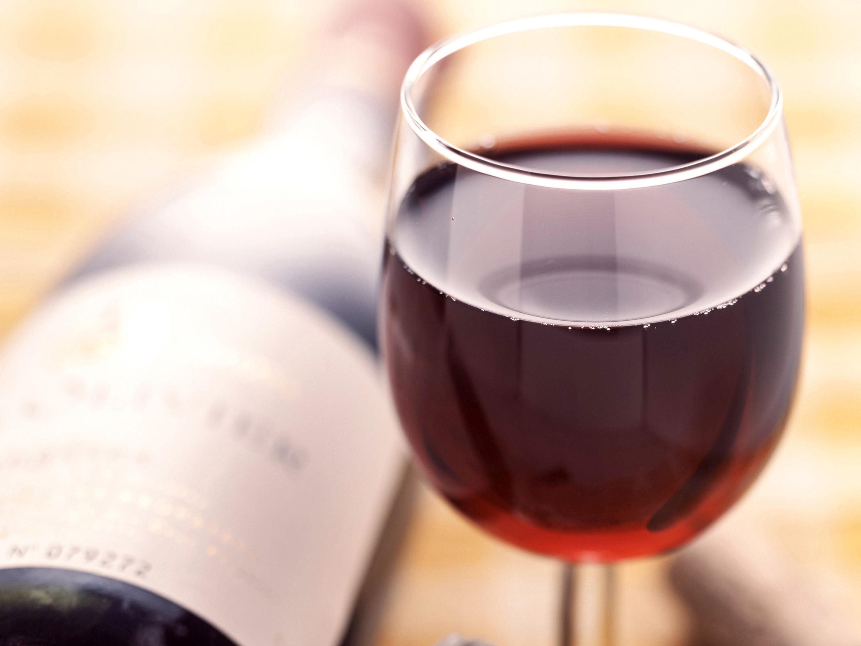 Una copa de vino tinto, una botella al fondo y un desenfoque de fondo.