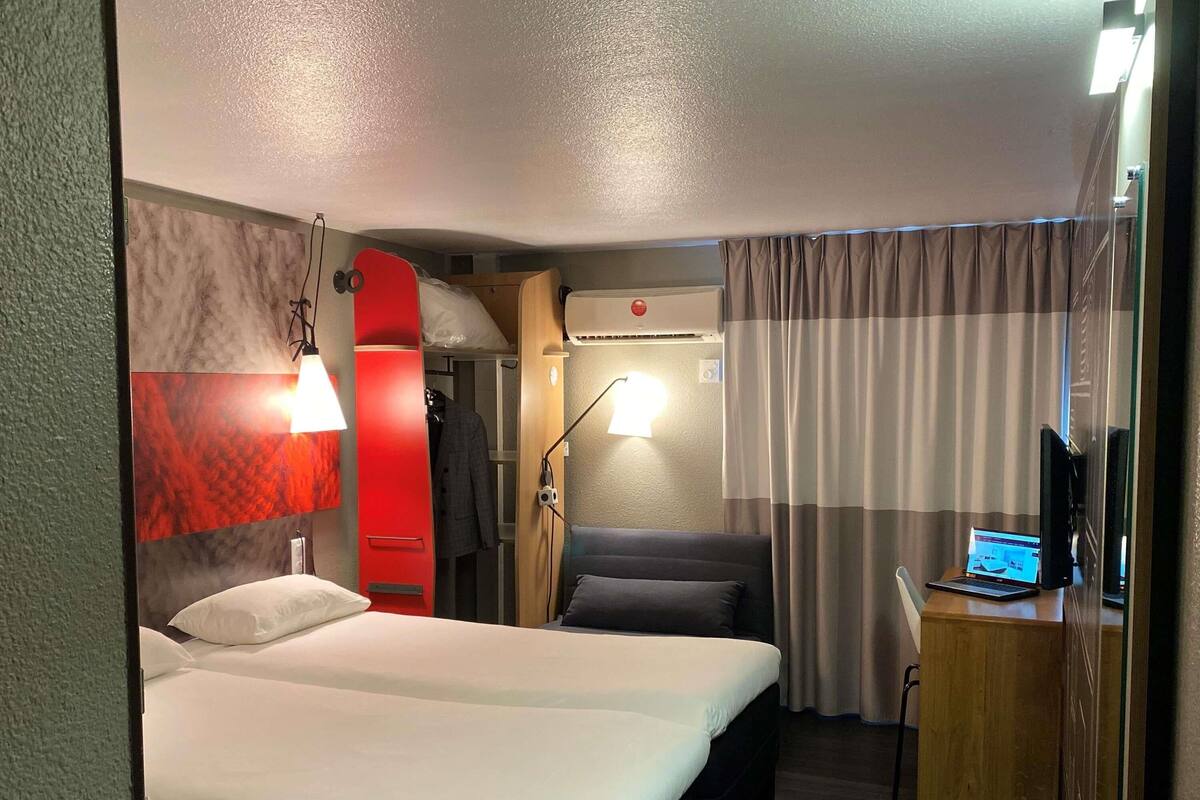 A hotel room with a bed, desk, chair, and a red cabinet.