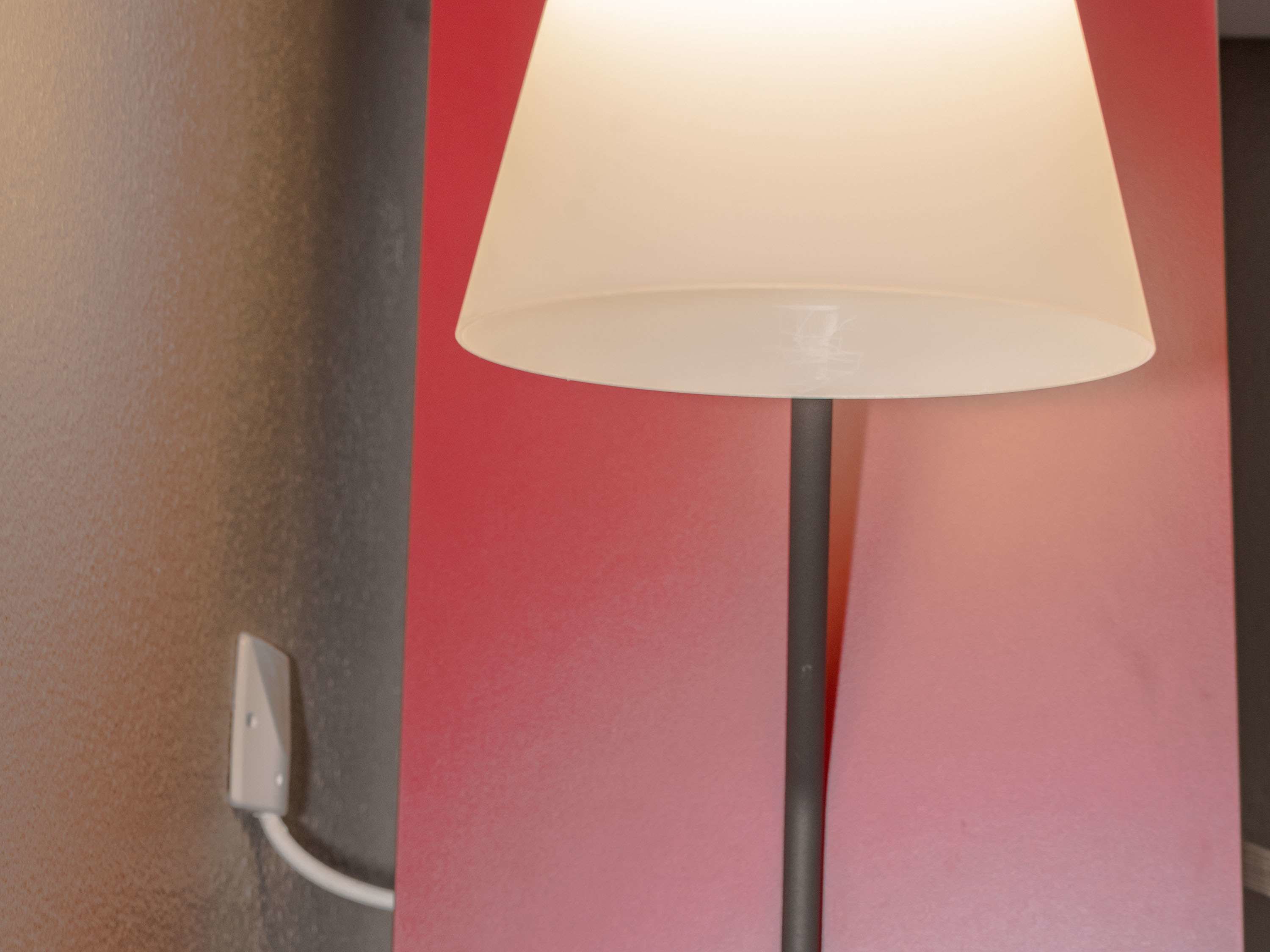 Eine Stehlampe mit weißem Lampenschirm vor einer roten Wand.