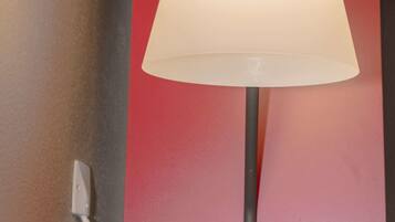 Eine Stehlampe mit weißem Lampenschirm vor einer roten Wand.