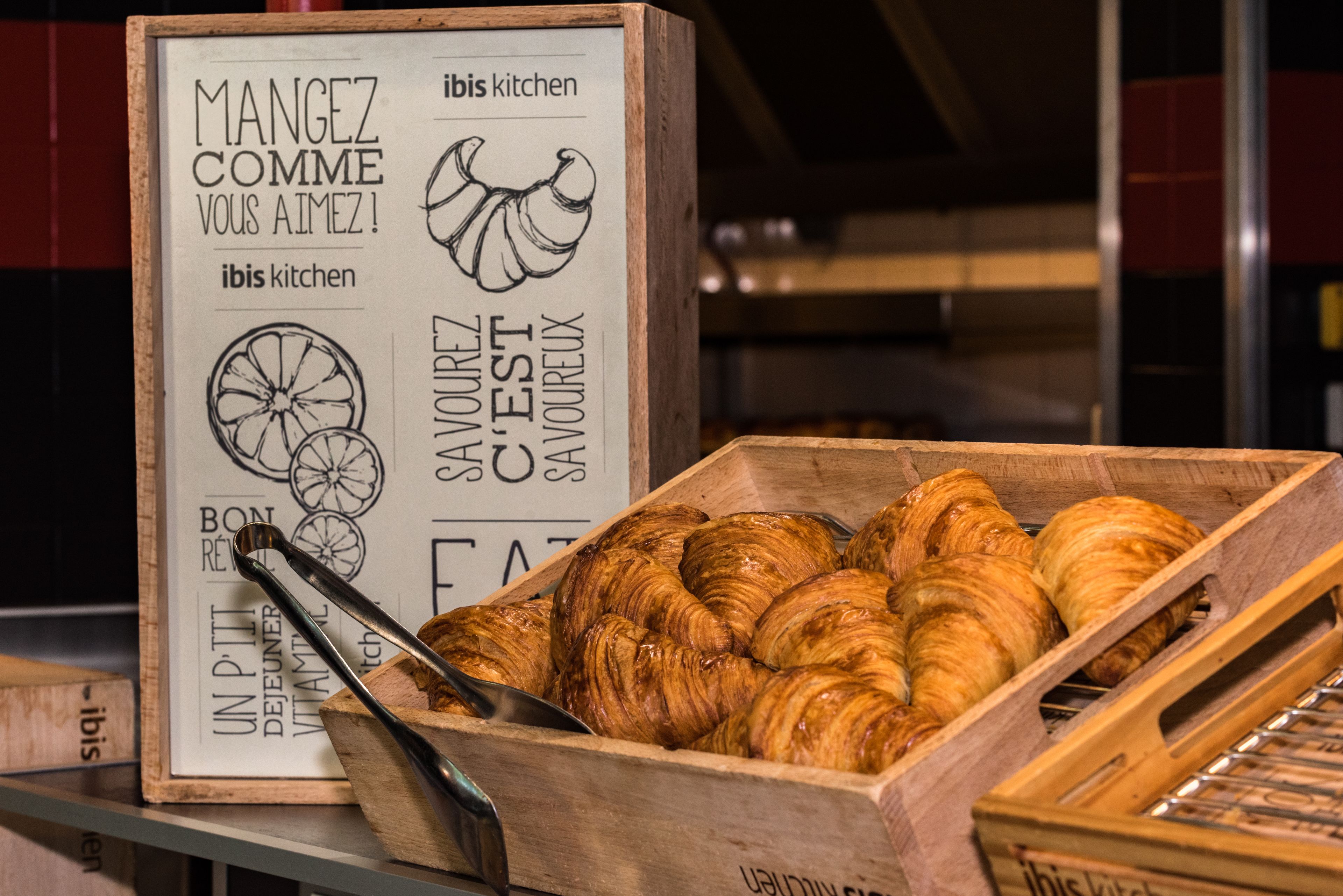 A wooden box filled with croissants and a sign with French text.