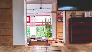 Una stanza con un tavolo di legno, un divano rosso, un tavolo da ping pong e una TV montata a parete.