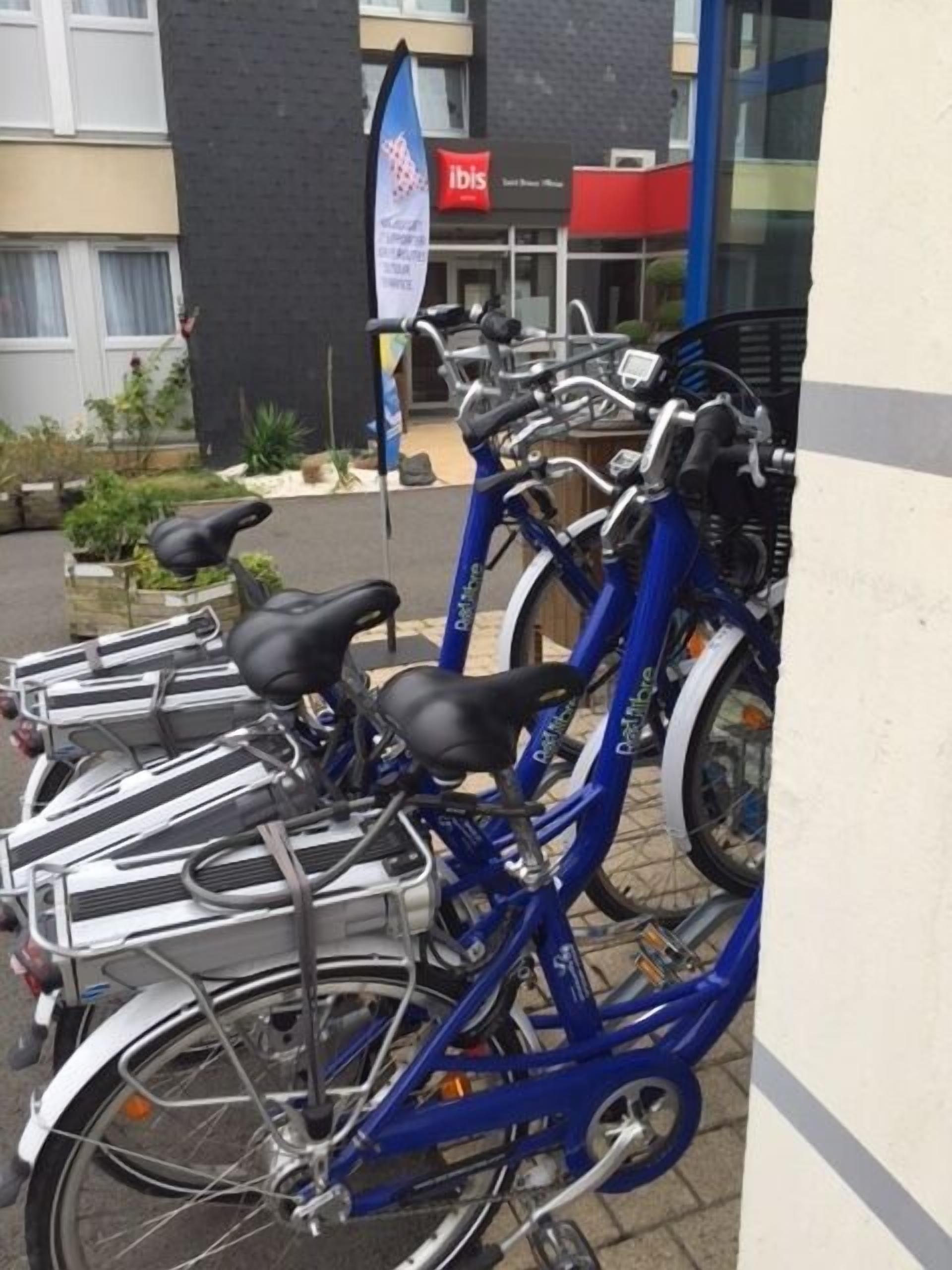 Eine Reihe blauer Fahrräder sind vor einem Gebäude abgestellt, an dem ein Schild mit der Aufschrift "ibis" hängt.