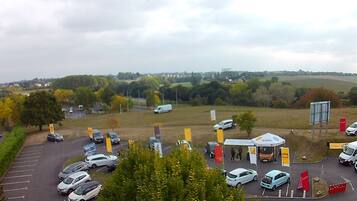 Ein Parkplatz mit mehreren Autos und einem Zeltbereich, umgeben von Bäumen und freier Feldlandschaft.