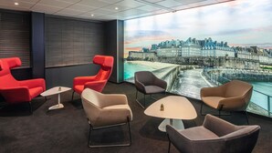 A modern lounge with a large window overlooking a historic cityscape. - ibis Saint Malo La Madeleine (Saint-Malo)