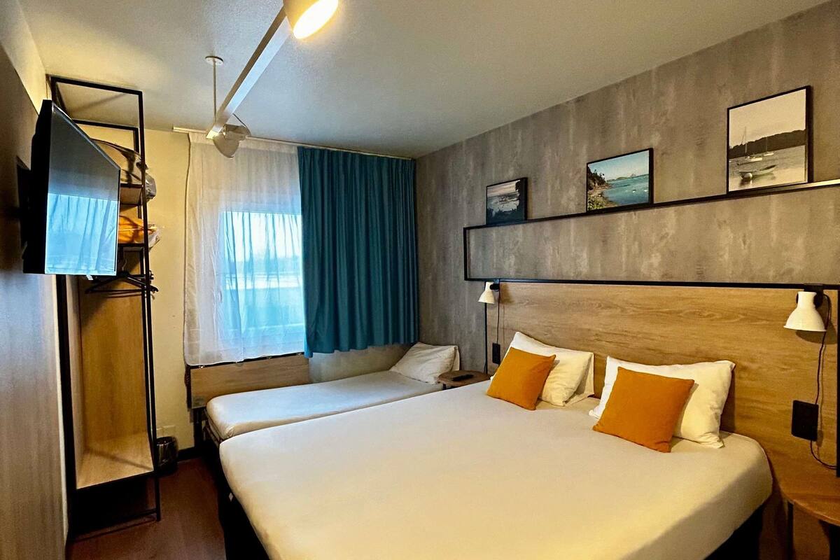 A hotel room with two beds, a TV, a ceiling fan, and artwork on the wall.