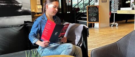 Une personne assise à une table, devant un menu, un magazine et une plante en pot.