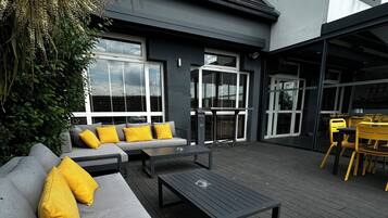 An outdoor seating area with a grey sofa, yellow cushions, and a black table.