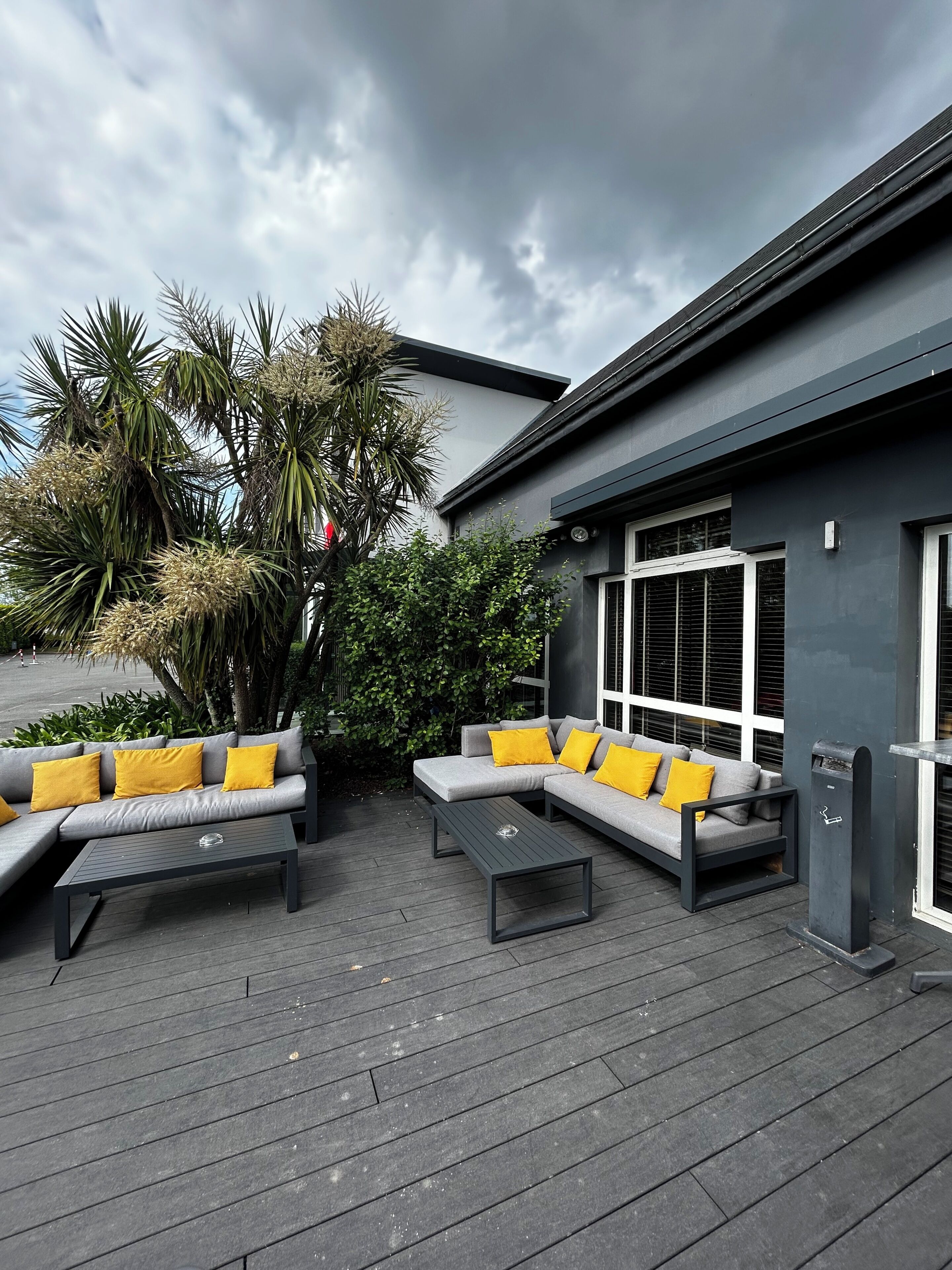 Un patio extérieur moderne avec un ensemble de canapés gris, des coussins jaunes et une table basse.
