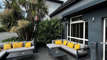 Un patio extérieur moderne avec un ensemble de canapés gris, des coussins jaunes et une table basse.