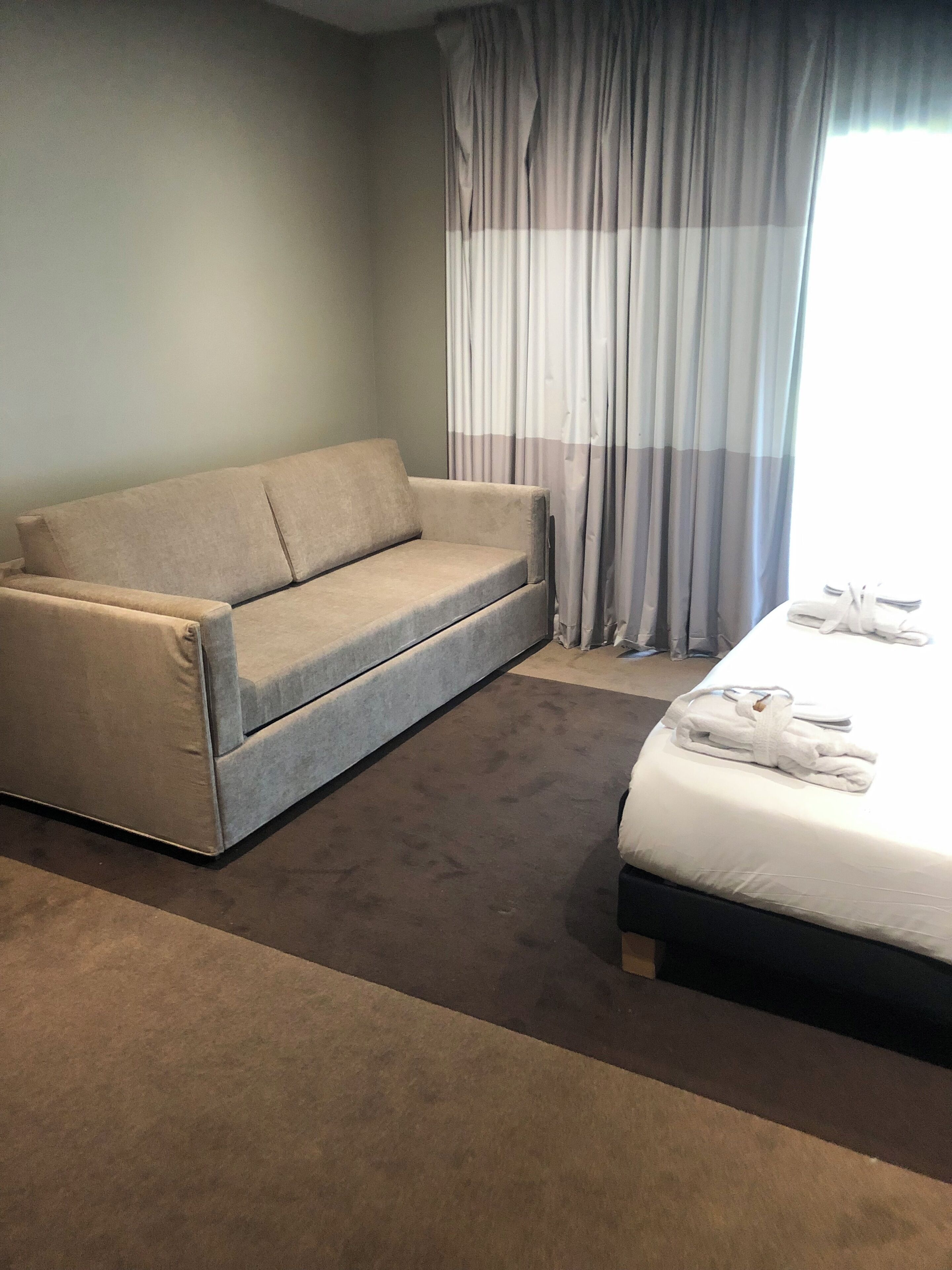 A hotel room with a sofa, a bed, and a window with curtains.
