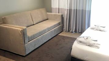A hotel room with a sofa, a bed, and a window with curtains.