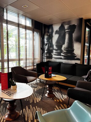 A modern lounge area with a round table, two chairs, a sofa, and a chessboard mural. - ibis Saint Malo La Madeleine (Saint-Malo)