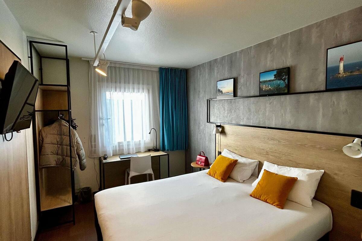 A hotel room with a bed, a desk, a chair, a TV, and a wardrobe.
