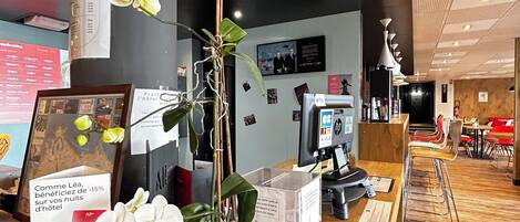 Un comptoir d’accueil agrémenté d’une plante en pot, d’un tableau encadré et de brochures d’information.