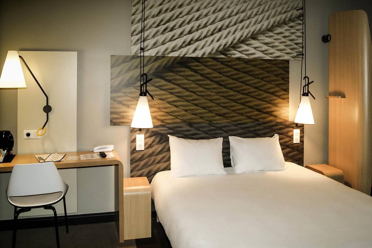 A hotel room with a bed, desk, chair, and two bedside lamps.