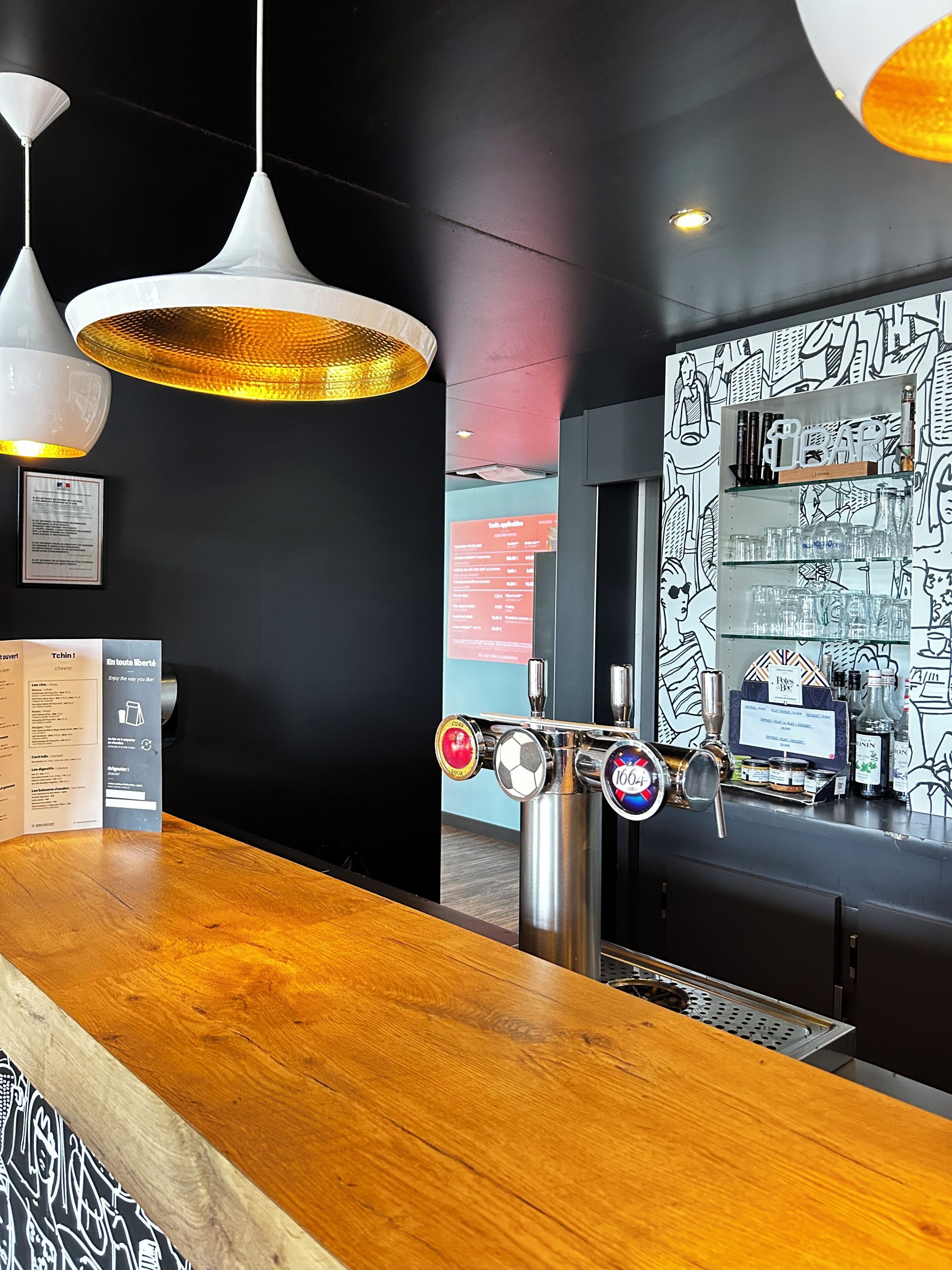 Un'area bar con un bancone in legno, una spina per la birra e una parete con illustrazioni in bianco e nero.