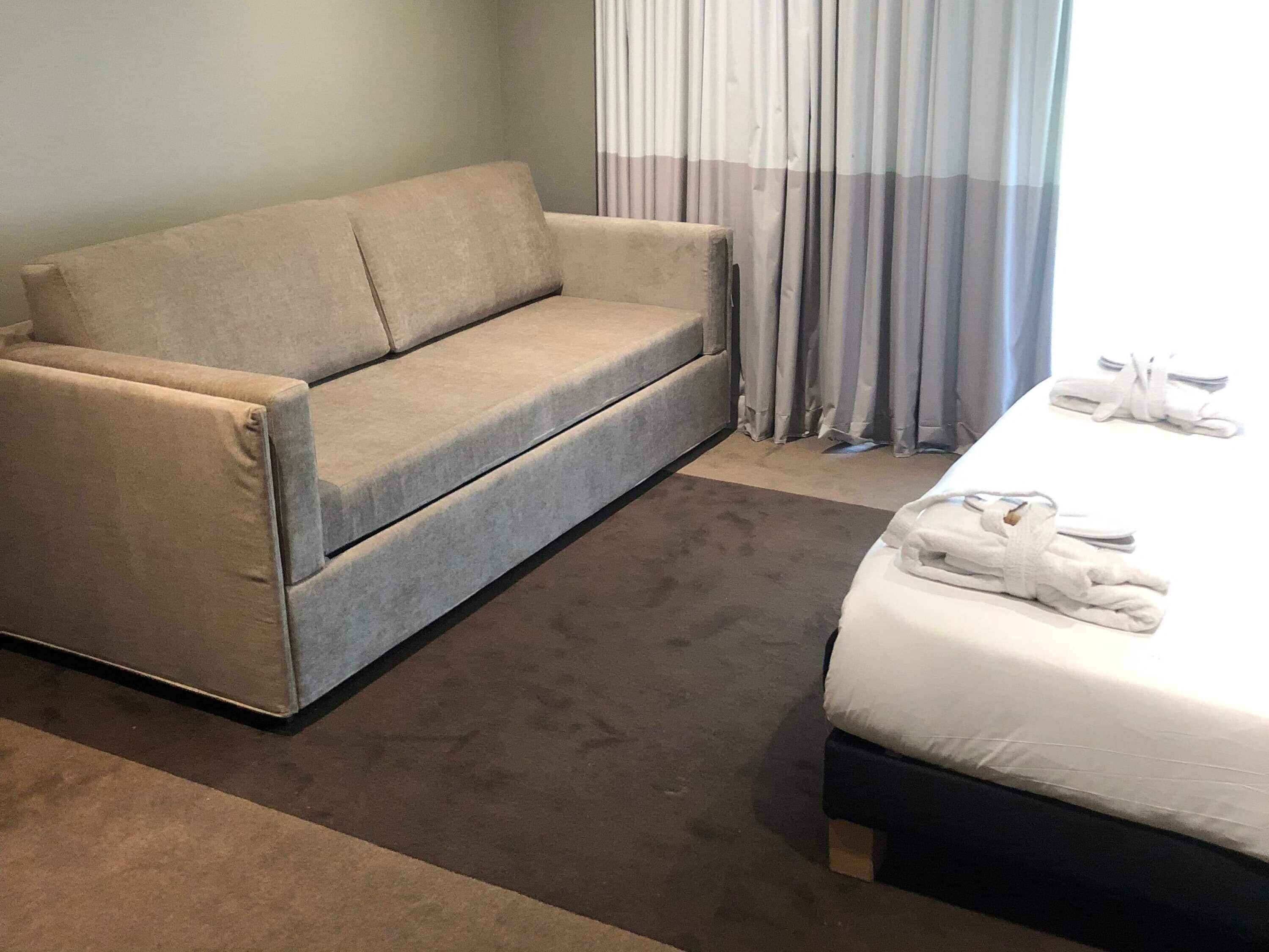 Ein Hotelzimmer mit Sofa, Bett, Teppichboden und einem Fenster mit Vorhängen.