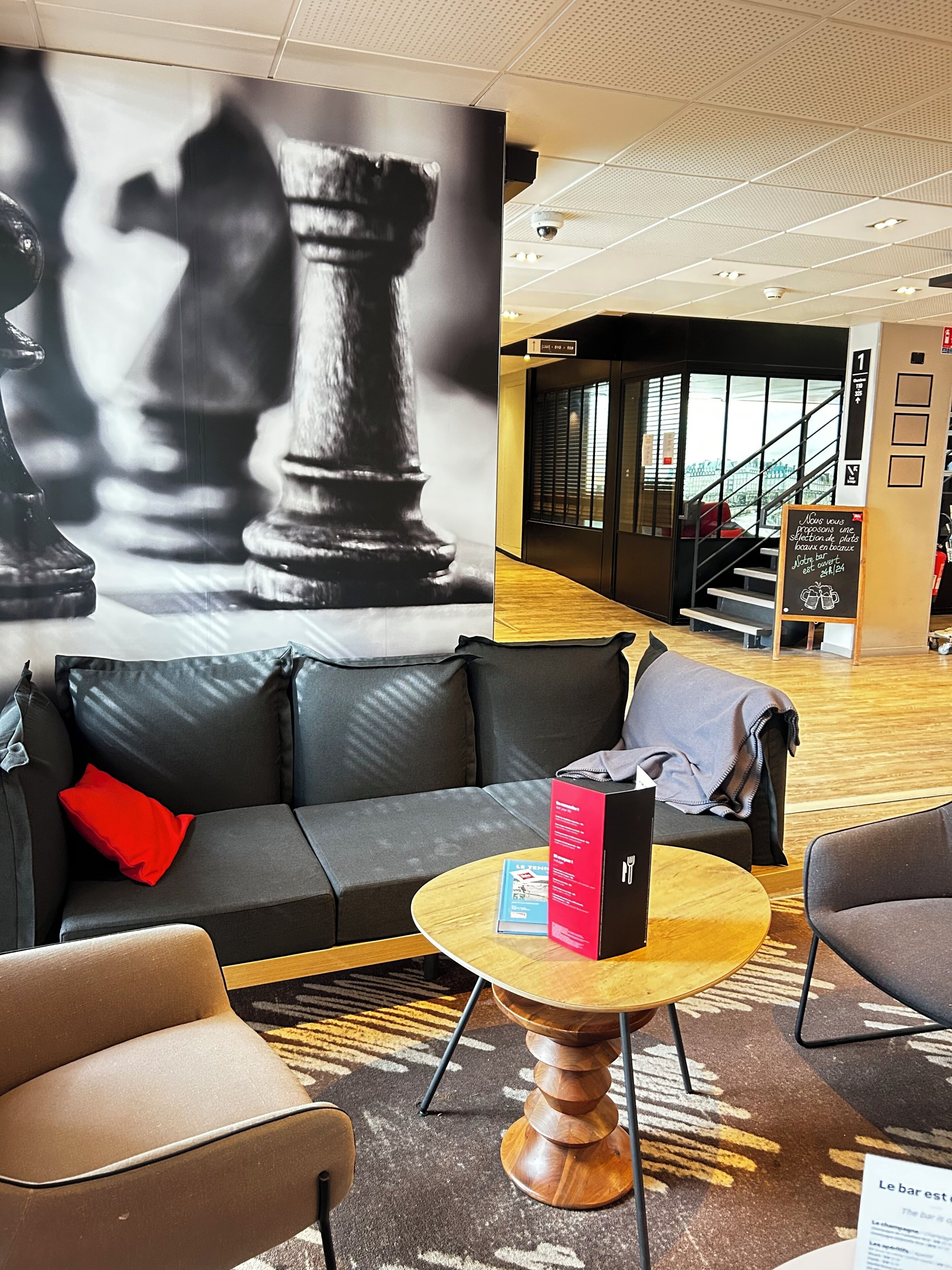 Eine moderne Lobby mit Wandgemälde von Schachfiguren in Schwarz-Weiß, einer Couch, einem Couchtisch und einer Treppe im Hintergrund.